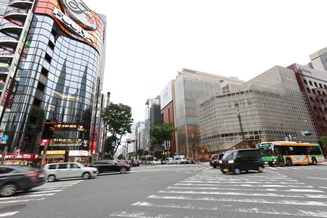A busy urban intersection with several vehicles, surrounded by tall buildings featuring glass and modern architecture