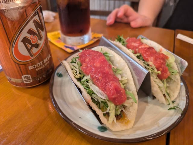 Two tacos filled with lettuce, meat, and topped with salsa on a plate, accompanied by a can of A&W root beer