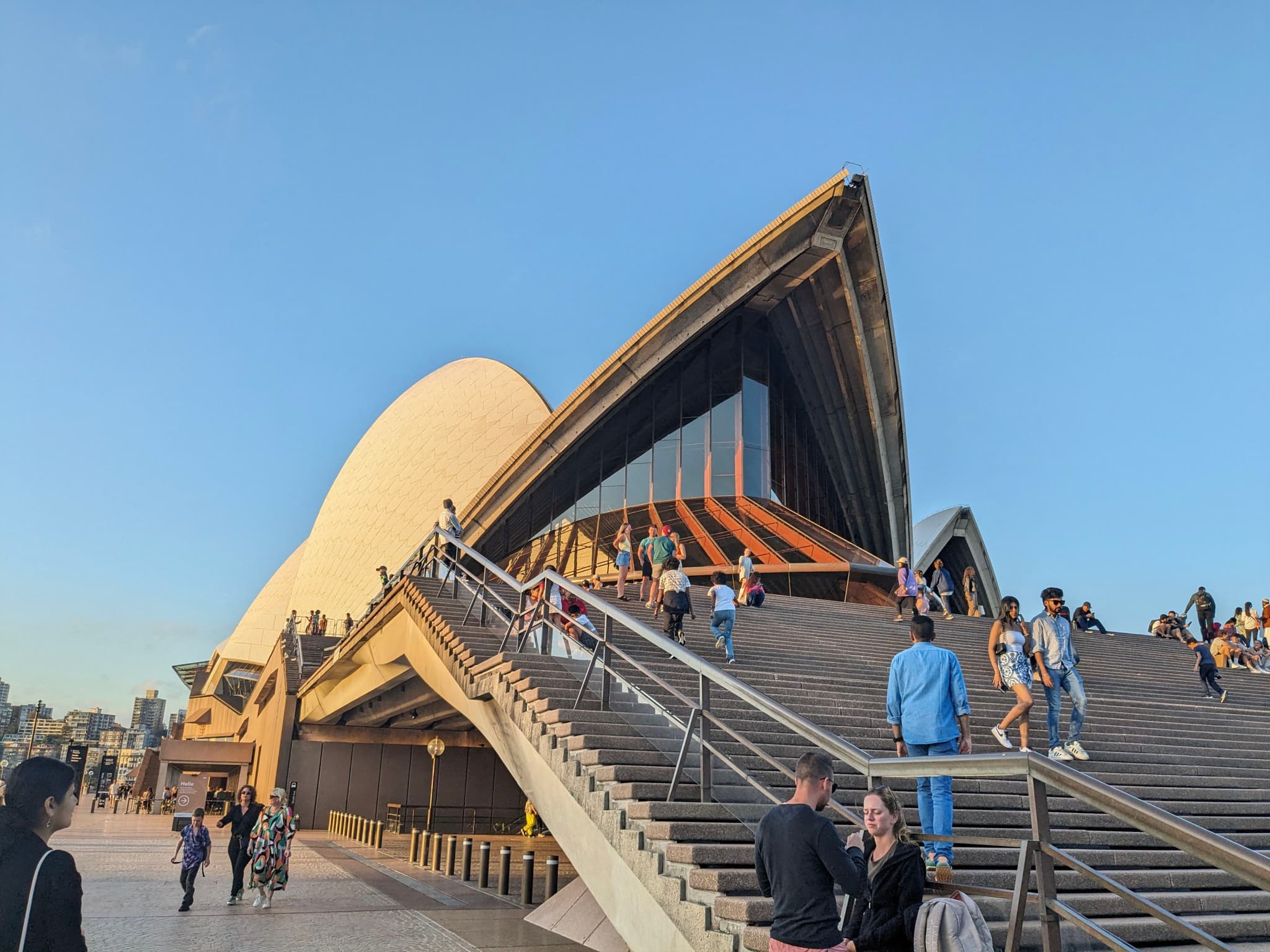 The Sydney Opera House with people walking on the steps and a clear blue sky in the background
