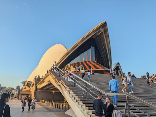 The Sydney Opera House with people walking on the steps and a clear blue sky in the background