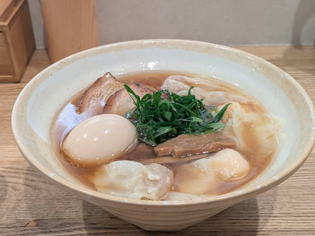 A bowl of ramen with sliced meat, a soft-boiled egg, green onions, and dumplings in broth