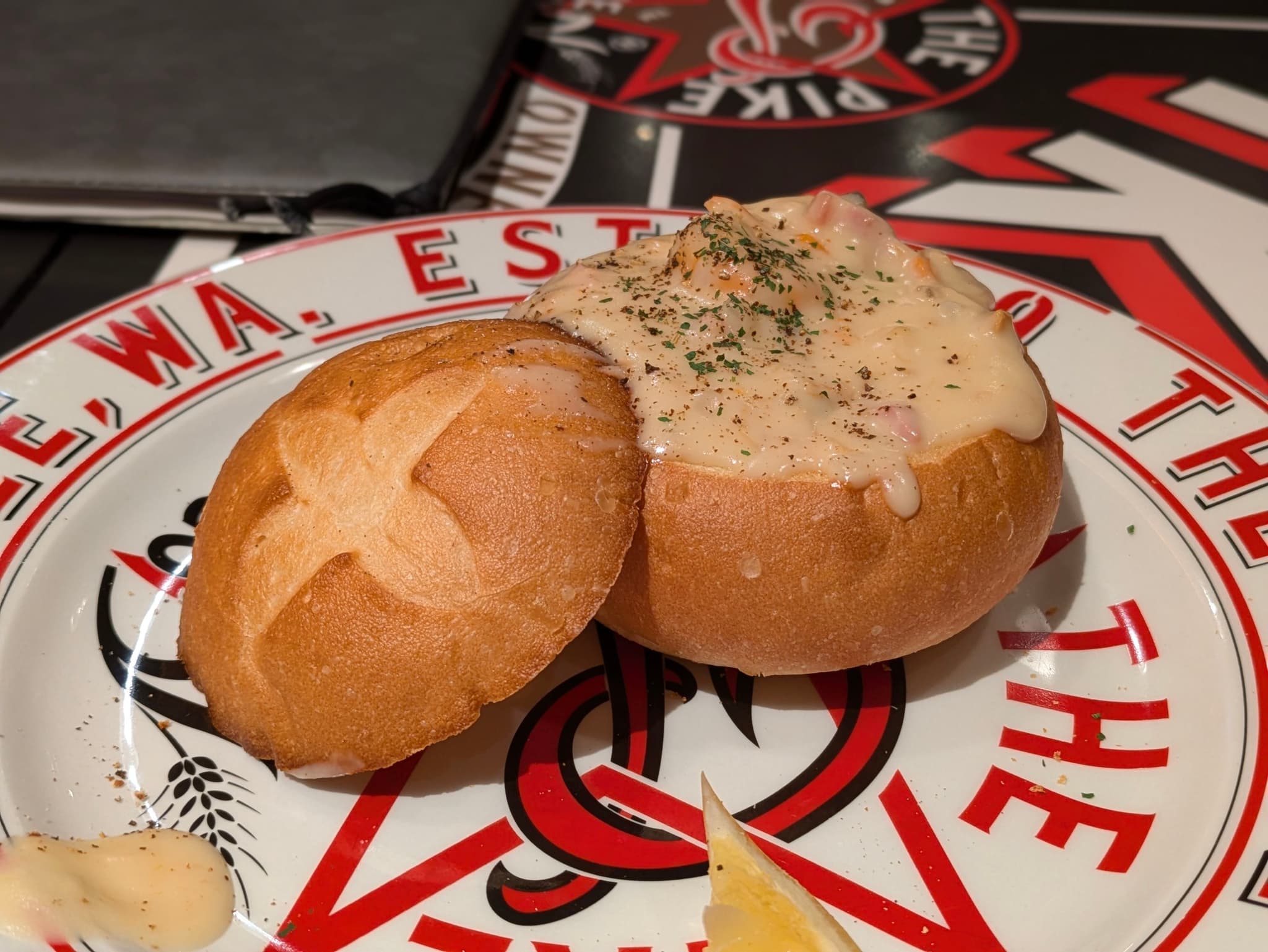 A bread bowl filled with creamy soup, garnished with herbs, placed on a decorative plate