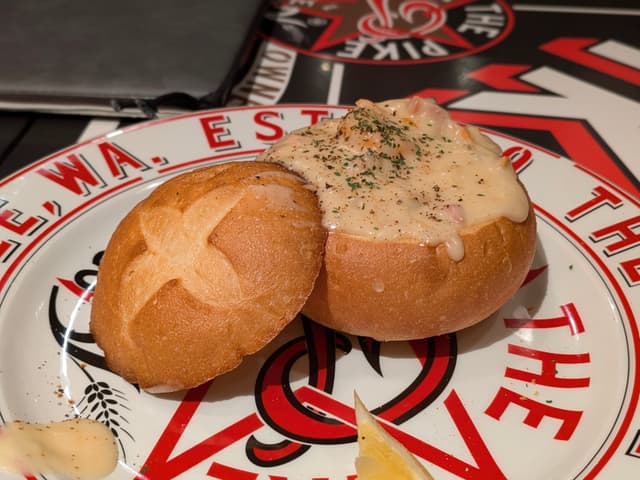 A bread bowl filled with creamy soup, garnished with herbs, placed on a decorative plate