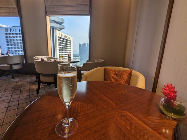 A glass of champagne on a wooden table in a modern dining area with large windows and cityscape views