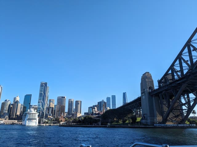 A city skyline with modern skyscrapers and a large bridge over a body of water under a clear blue sky