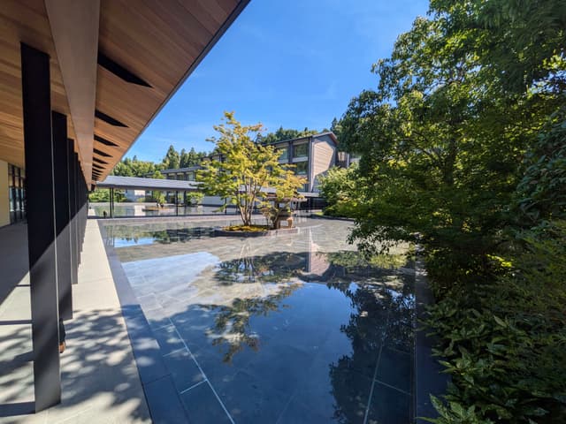 A modern architectural structure with a reflective water feature, surrounded by lush greenery and a clear blue sky